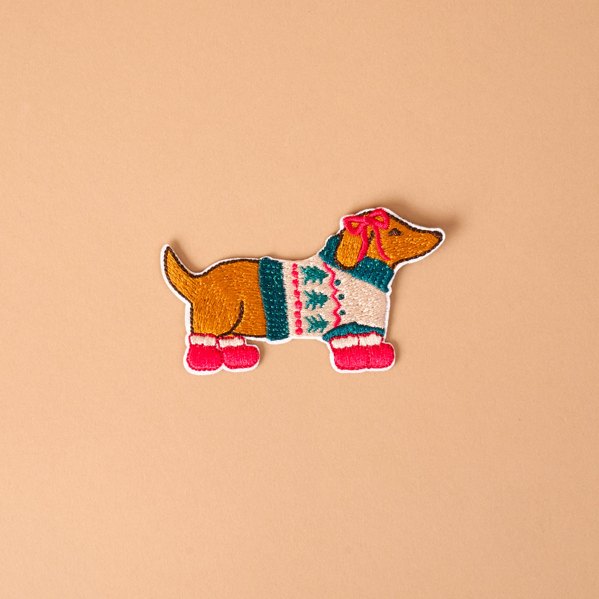 Dashing Dachshund Mix & Match Iron-On Patch featuring a dachshund wearing a tree-patterned sweater, a pink ear bow, and pink boots.