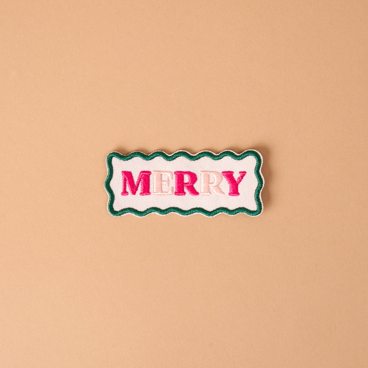 Merry Mix & Match Iron-On Patch featuring a rectangular shape with wavy green edges and the word MERRY in pink embroidered letters on a white background.