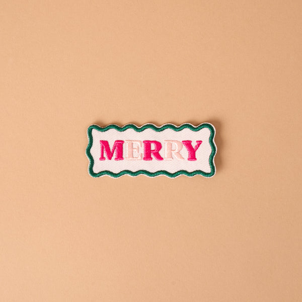 Merry Mix & Match Iron-On Patch featuring a rectangular shape with wavy green edges and the word MERRY in pink embroidered letters on a white background.