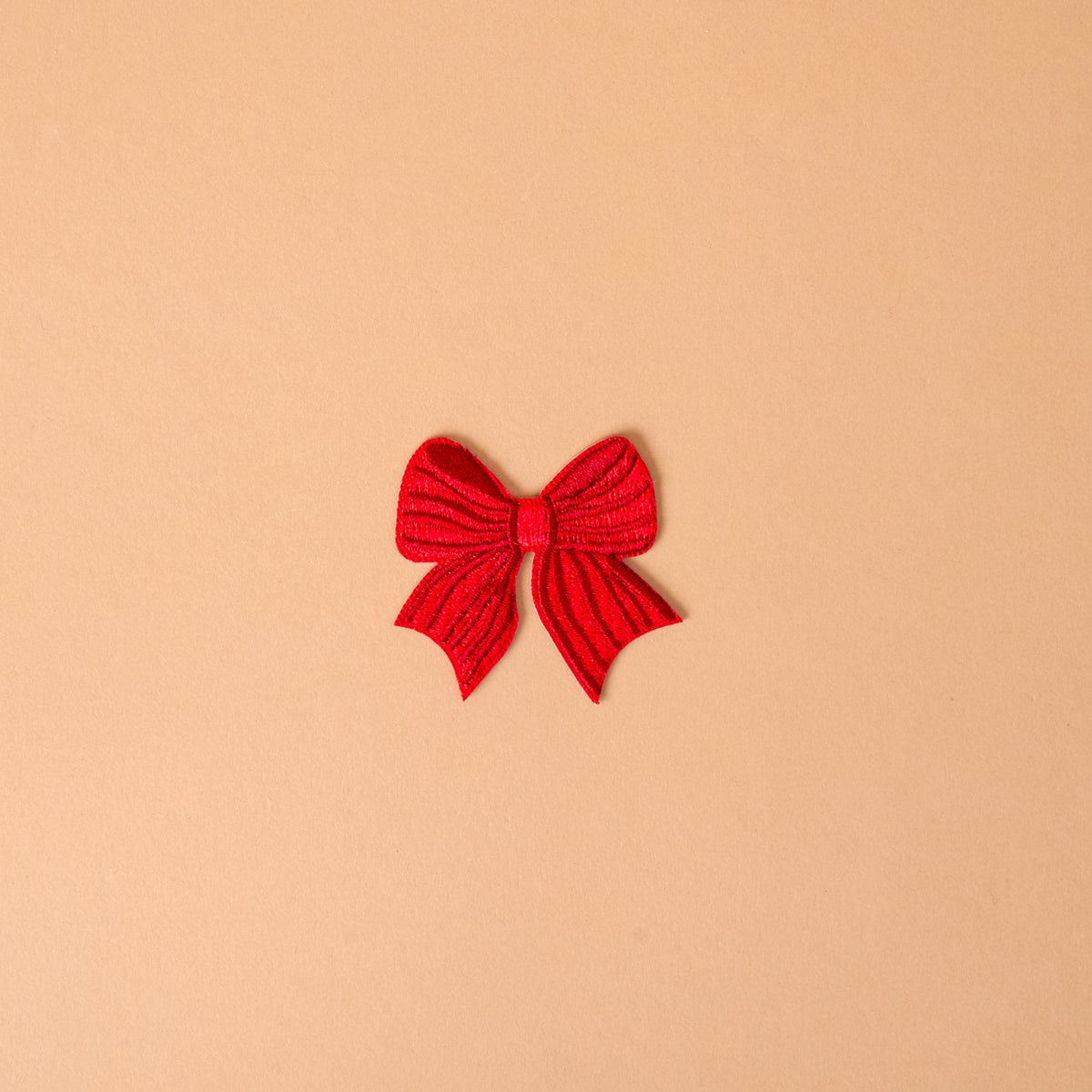 A red bow-shaped Red Bow Mix & Match Iron-On Patch used to customize jackets.