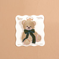Teddy Bear Theo Mix & Match Iron-On Patch featuring an embroidered teddy bear with a dark green bow, attached to a branded display card.