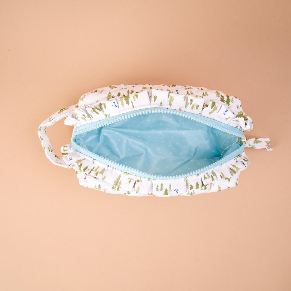 The Aprés Ski Essentials Quilted Cosmetic Pouch is an open, quilted bag featuring a winter pine tree and skier pattern with a light blue interior.