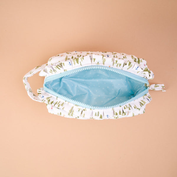 The Aprés Ski Essentials Quilted Cosmetic Pouch is an open, quilted bag featuring a winter pine tree and skier pattern with a light blue interior.
