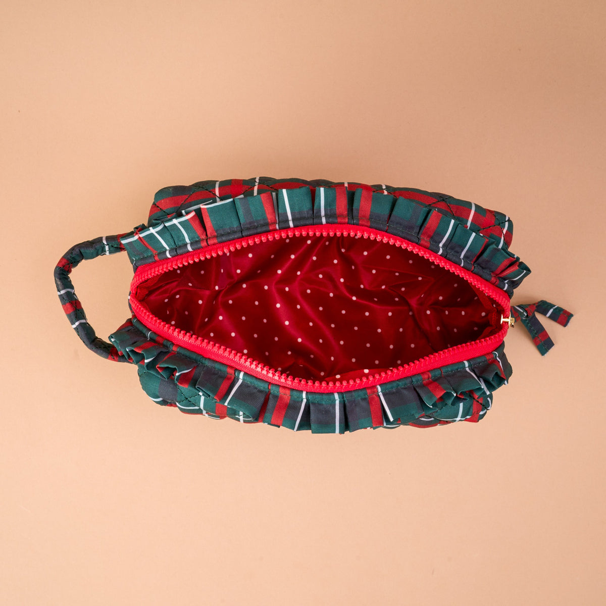 The Evergreen Plaid Essentials Quilted Cosmetic Pouch is an open, green and red plaid quilted bag with ruffled edges and a red interior featuring a white polka dot print.