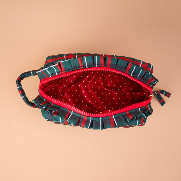 The Evergreen Plaid Essentials Quilted Cosmetic Pouch is an open, green and red plaid quilted bag with ruffled edges and a red interior featuring a white polka dot print.