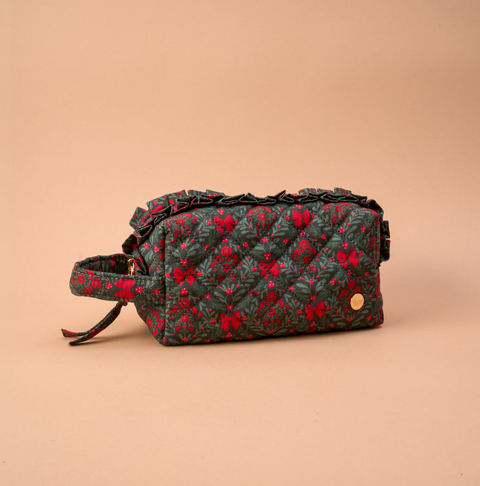 A Merry Moment Essentials Quilted Cosmetic Pouch featuring a dark green pattern of red berries and bows, with a ruffled top edge and a side carry strap.
