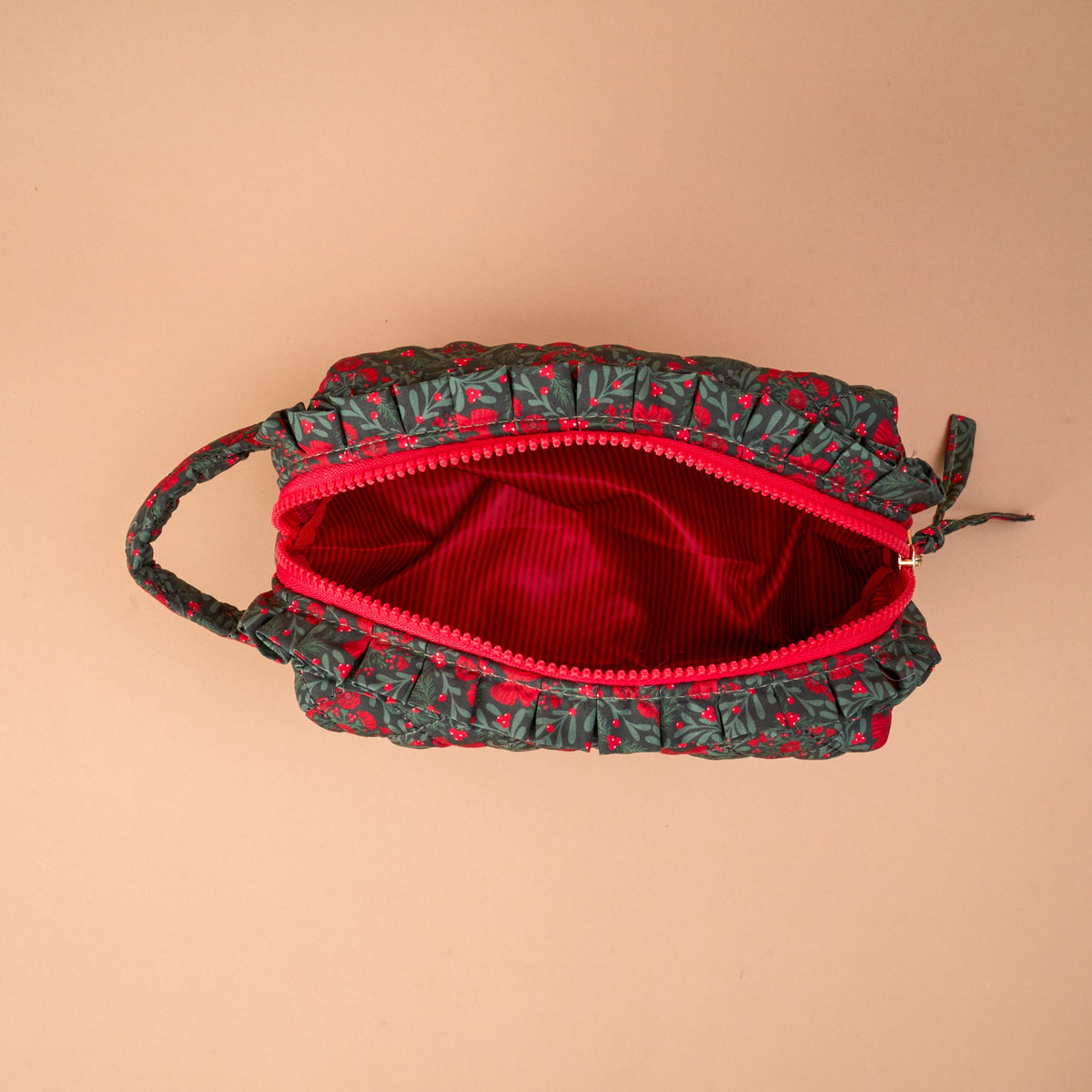 A Merry Moment Essentials Quilted Cosmetic Pouch in a red floral pattern with a ruffle trim, an open top, and a bright red interior lining.