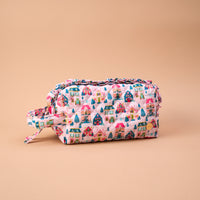Sugarplum Lane Essentials Quilted Cosmetic Pouch in pink with a print of colorful holiday houses and pine trees, featuring ruffled trim and a side carry handle.