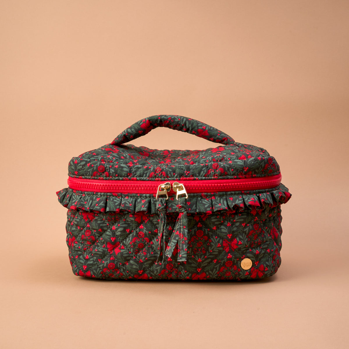 A Merry Moment Glam & Go Quilted Cosmetic Bag in a dark green holiday floral print with a red ruffled trim and dual gold zippers, serving as a stylish travel makeup bag.