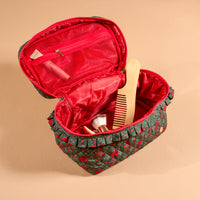 Open quilted dark green A Merry Moment Glam & Go Quilted Cosmetic Bag with a red holly print and a ruffled trim, containing a wooden comb and makeup brushes.