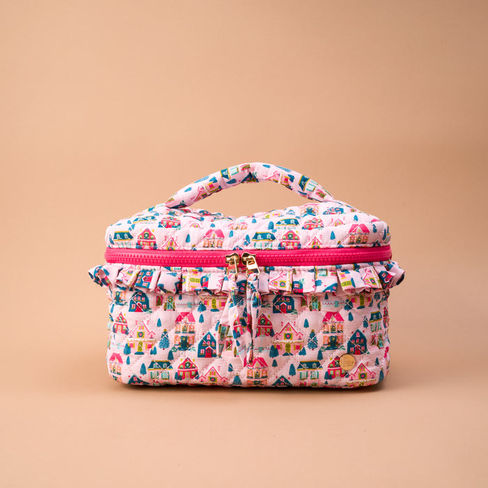 Sugarplum Lane Glam & Go Quilted Cosmetic Bag featuring a pink, light blue, and house pattern with a ruffled zipper trim and top handle, perfect as a travel makeup bag.