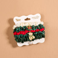 Evergreen Plaid Scrunchie Charm Set featuring four stylish hair accessories in white, dark green, and red, attached to a display card with a small gift box charm and a teddy bear charm.
