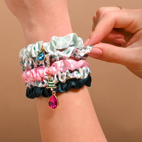 A hand wears the Sugarplum Lane Scrunchie Charm Set, a collection of four scrunchies featuring teardrop and Christmas tree charms.