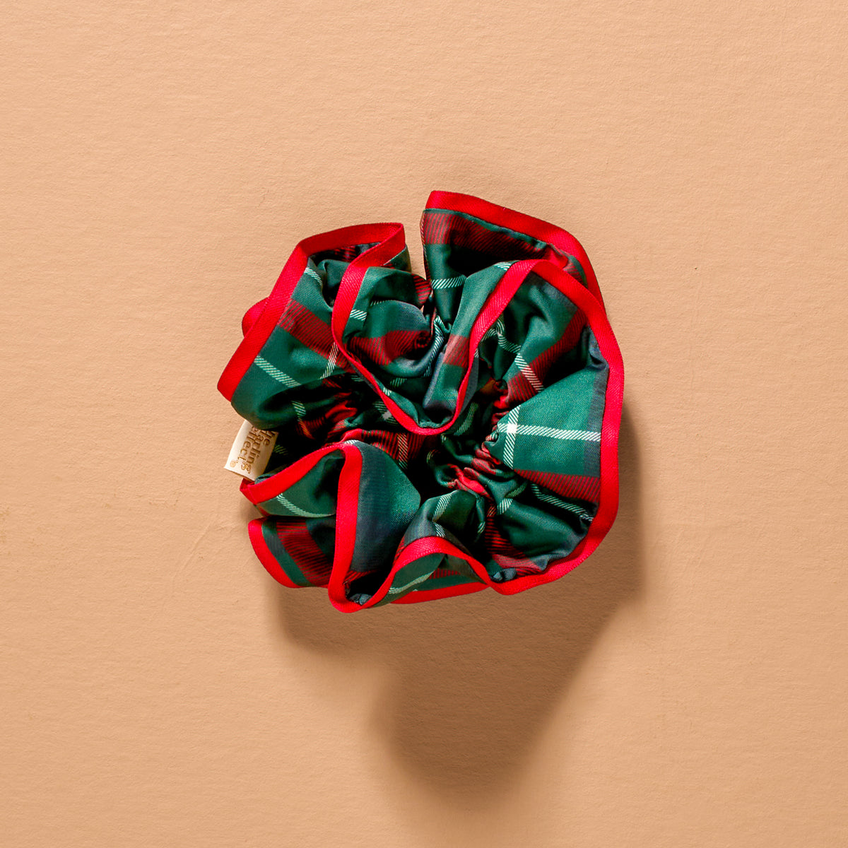 An Evergreen Plaid Ruffle Up Scrunchie featuring an oversized, ruffled design in a green, red, and white plaid pattern with a bright red edge.
