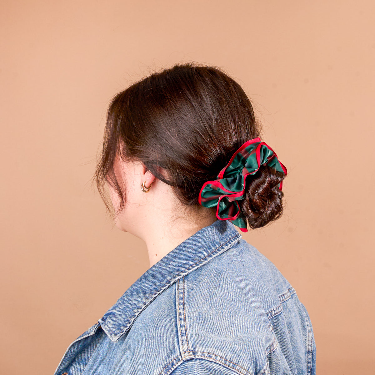 A person with brown hair in a low bun secured by an oversized, ruffled green and red plaid Evergreen Plaid Ruffle Up Scrunchie from The Darling Effect.
