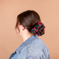 A person with brown hair in a low bun secured by an oversized, ruffled green and red plaid Evergreen Plaid Ruffle Up Scrunchie from The Darling Effect.