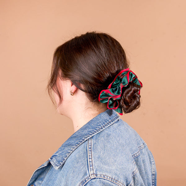 A person with brown hair in a low bun secured by an oversized, ruffled green and red plaid Evergreen Plaid Ruffle Up Scrunchie from The Darling Effect.