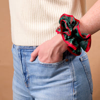 An Evergreen Plaid Ruffle Up Scrunchie worn around a wrist, featuring an oversized, ruffled design in green and red plaid with a solid red trim.