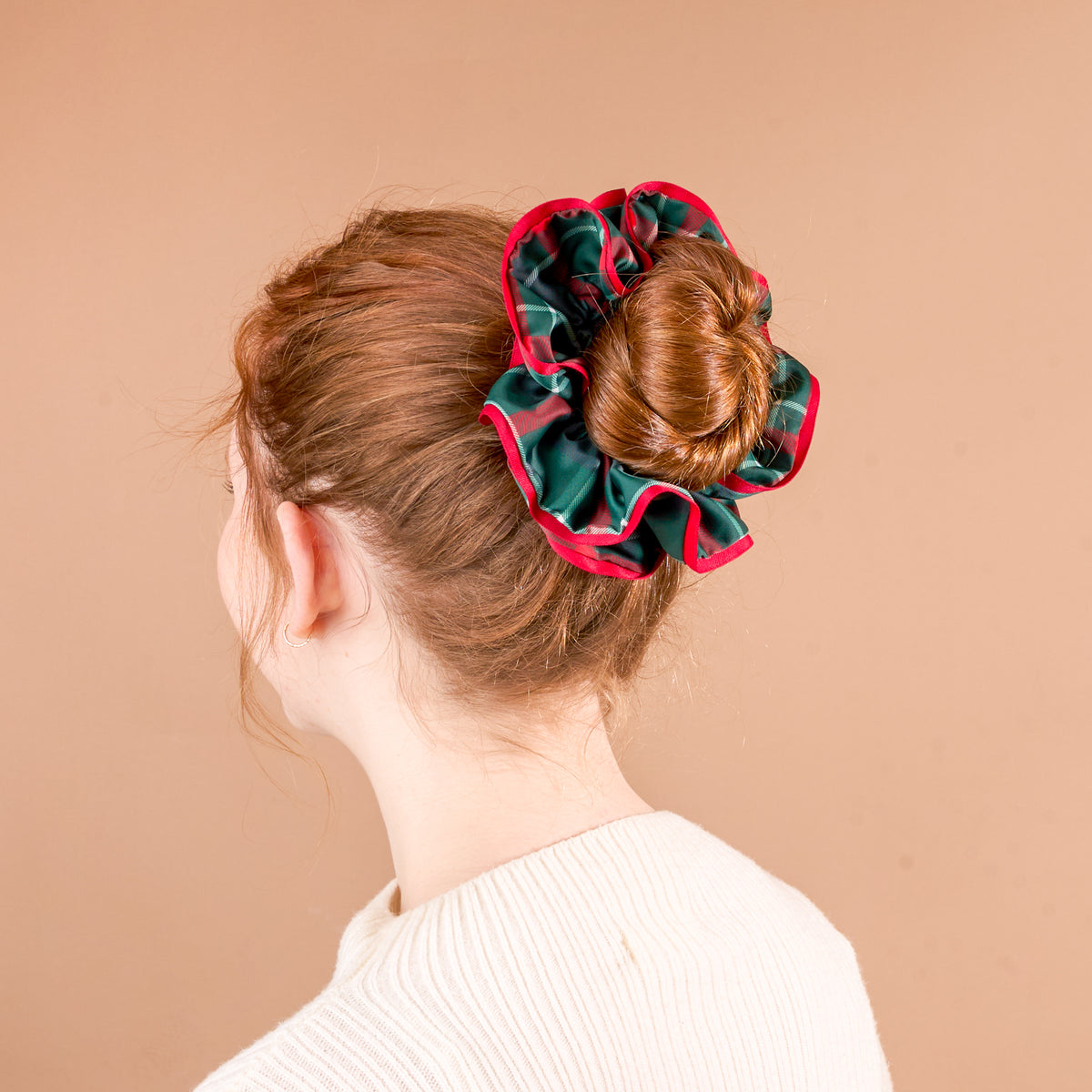 A person with their hair in a bun secured by an oversized, green and red plaid Evergreen Plaid Ruffle Up Scrunchie.