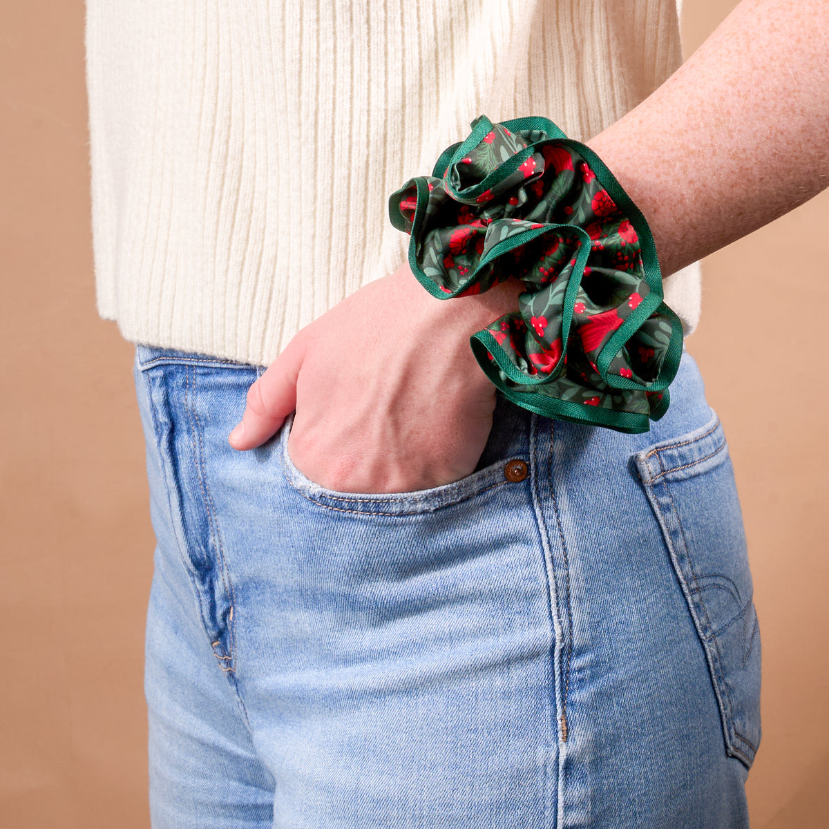 A Merry Moment Ruffle Up Scrunchie by The Darling Effect, featuring an oversized, ruffled design with a festive pattern of red berries and green leaves worn around a wrist.
