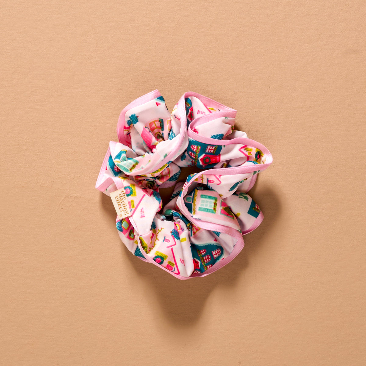 Sugarplum Lane Ruffle Up Scrunchie featuring an oversized ruffle design with a colorful house and tree pattern and a pink edge.