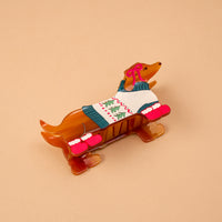 The Dashing Dachshund Shape Up Claw Clip is a brown hair clip shaped like a dachshund wearing a Christmas sweater and red mittens.