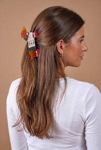 A Dashing Dachshund Shape Up Claw Clip in brown, featuring a white sweater design with green trees, shown holding hair in a cute half-up hairstyle.