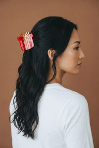 A woman wears a Holiday Gift Shape Up Claw Clip shaped like a red gift box with a gold ribbon.