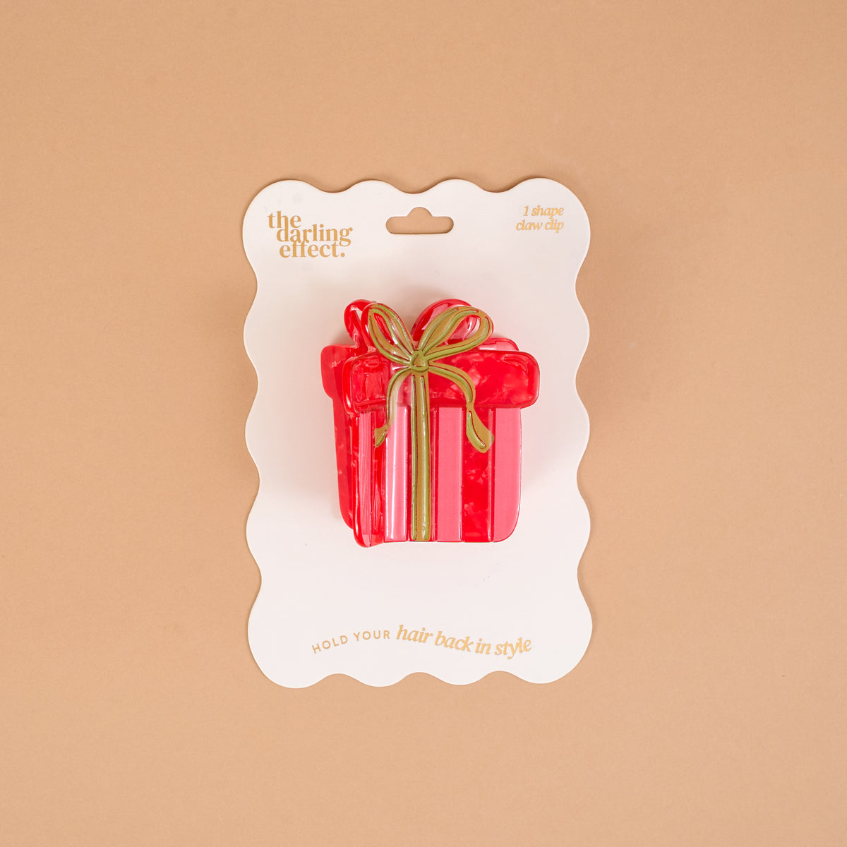 A Holiday Gift Shape Up Claw Clip in red with a gold ribbon design, mounted on a white display card as a cute hair accessory.