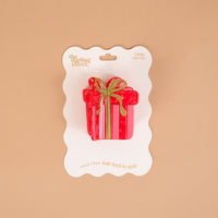 A Holiday Gift Shape Up Claw Clip in red with a gold ribbon design, mounted on a white display card as a cute hair accessory.