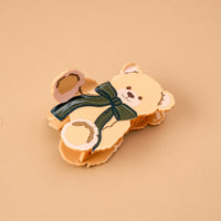 Teddy Bear Theo Shape Up Claw Clip in tan, shaped like a bear and adorned with a dark green bow.