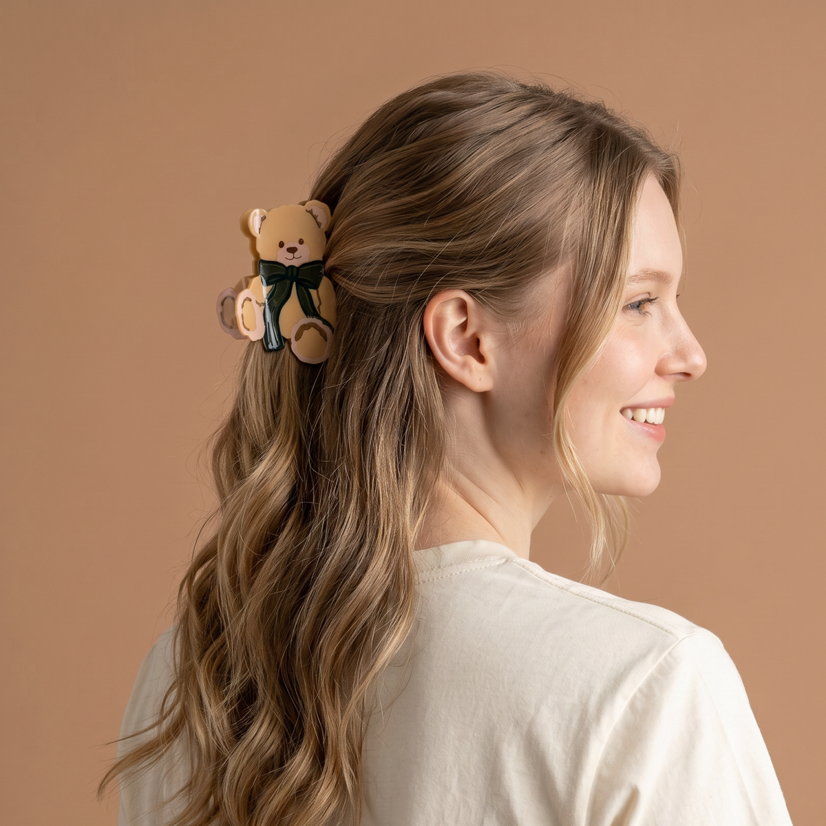 A smiling woman wears a cute hairstyle featuring a Teddy Bear Theo Shape Up Claw Clip in the shape of a teddy bear with a dark green bow.