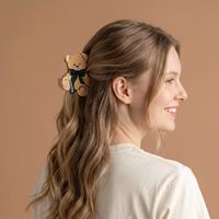 A smiling woman wears a cute hairstyle featuring a Teddy Bear Theo Shape Up Claw Clip in the shape of a teddy bear with a dark green bow.