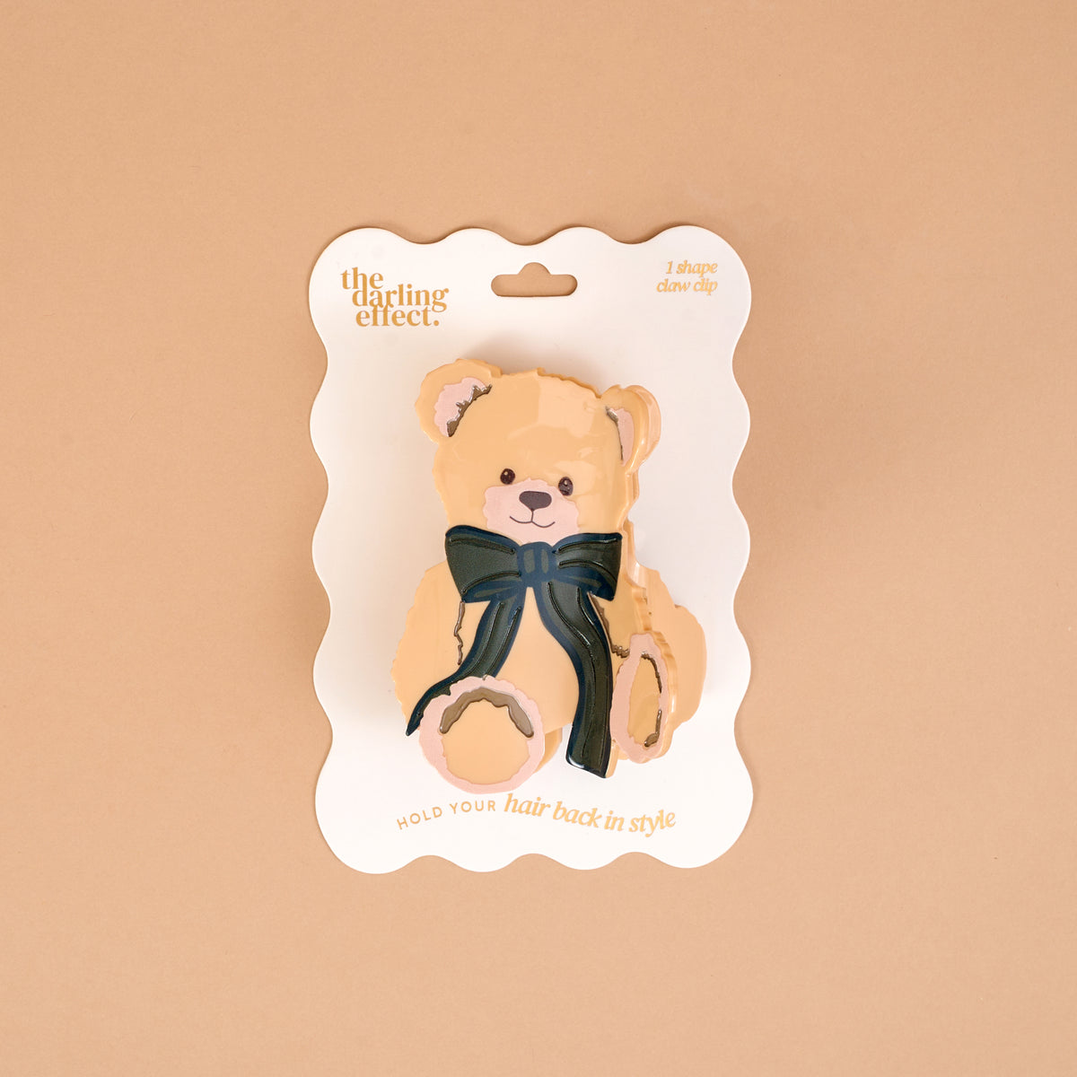 Teddy Bear Theo Shape Up Claw Clip shaped like a teddy bear and adorned with a dark green bow on a branded display card.