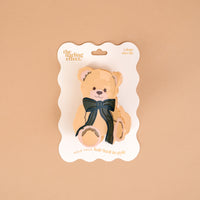Teddy Bear Theo Shape Up Claw Clip shaped like a teddy bear and adorned with a dark green bow on a branded display card.