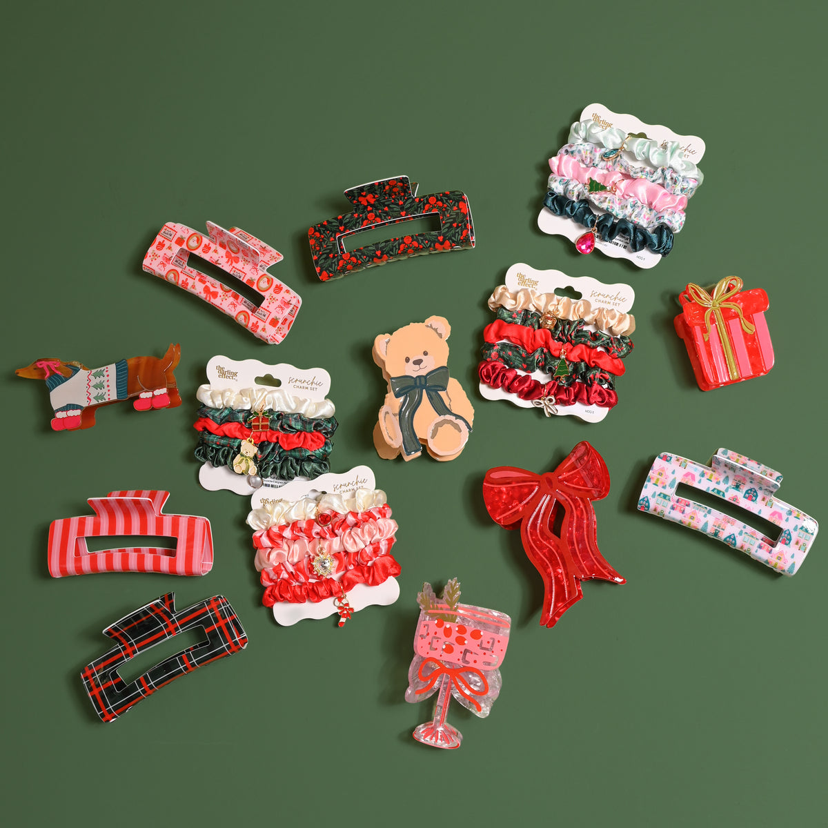 A collection of holiday-themed hair accessories, including the Teddy Bear Theo Shape Up Claw Clip, alongside other clips in shapes like bows, presents, and dachshunds, and sets of assorted scrunchies.