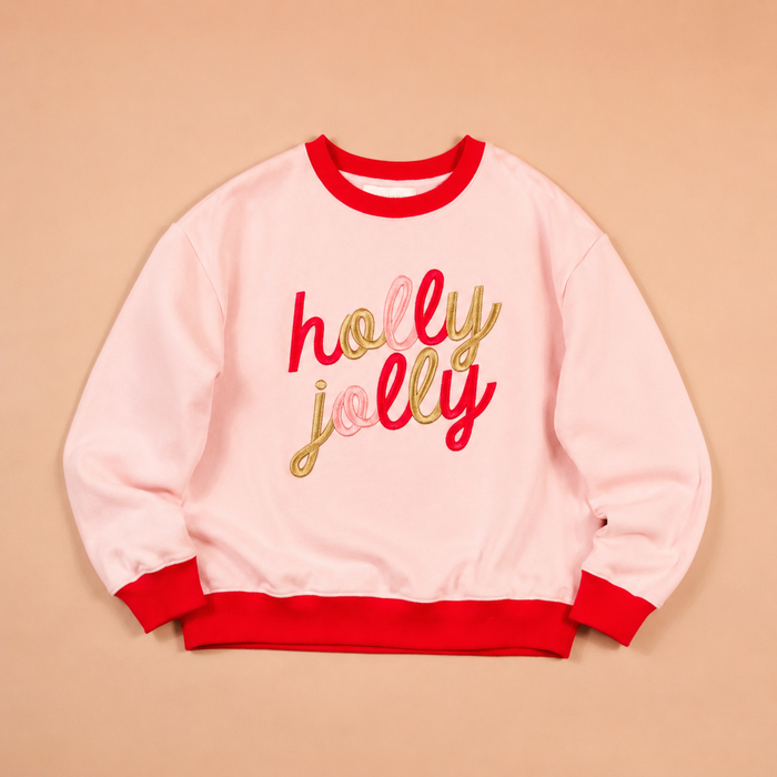 The Darling Effect Holly Jolly Signature Crew is a soft, light pink sweatshirt with red neck and cuff trim, featuring holly jolly embroidered in gold and red script across the chest.