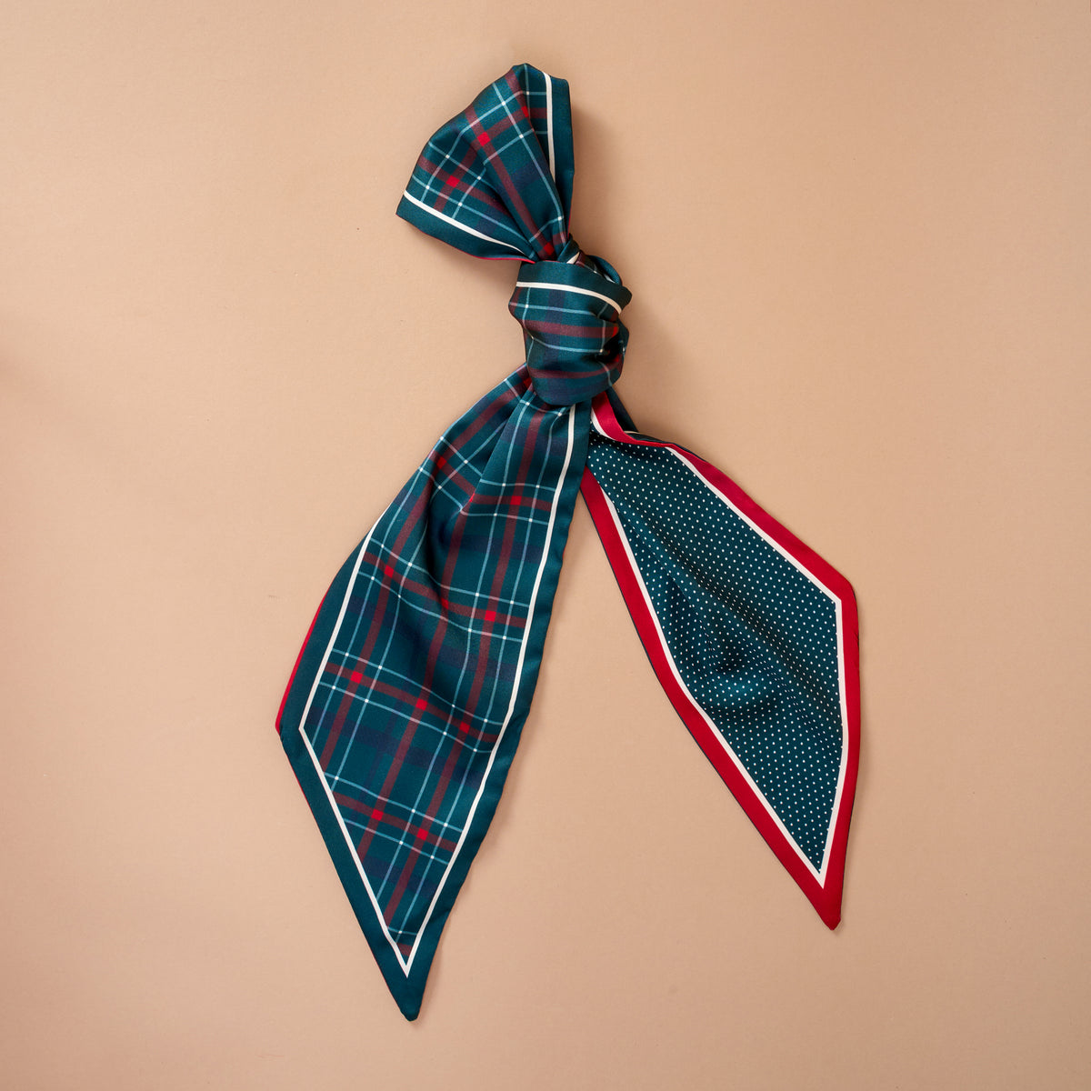 The Evergreen Plaid Twirl & Tie Scarf Accessory is a satin scarf tied with one end in a green and red plaid pattern and the other in a blue and white polka dot pattern with a red border, offering versatile styling options.
