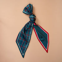 The Evergreen Plaid Twirl & Tie Scarf Accessory is a satin scarf tied with one end in a green and red plaid pattern and the other in a blue and white polka dot pattern with a red border, offering versatile styling options.