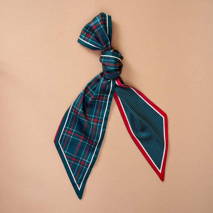 The Evergreen Plaid Twirl & Tie Scarf Accessory is a satin scarf tied with one end in a green and red plaid pattern and the other in a blue and white polka dot pattern with a red border, offering versatile styling options.