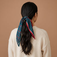 A person seen from behind wears their dark hair in a low ponytail tied with an Evergreen Plaid Twirl & Tie Scarf Accessory, featuring green plaid on one side and navy blue polka dots with red trim on the other.