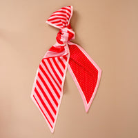 The Peppermint Stripes Twirl & Tie Scarf Accessory by The Darling Effect is a red and pink satin scarf tied in a knot, featuring one side with diagonal stripes and the other with a white polka dot pattern.