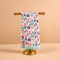 Sugarplum Lane Waffle Tea Towel featuring a repeating print of colorful holiday cottages and evergreen trees hanging on a gold towel stand.