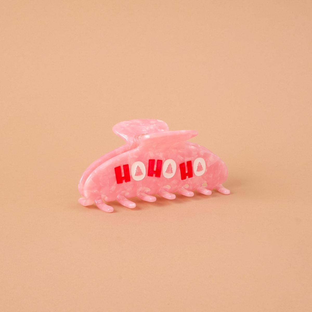 The Darling Effect Ho Ho Ho Word Up Claw Clip is a pink marbled hair accessory featuring red HO HO HO text and small tree icons.