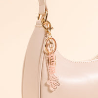 Close-up of a cream-colored handbag with a gold clasp, featuring the-darling-effect's Mom Life Acrylic Keychain attached to the strap.