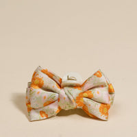 The Darling Effect’s Bouquet Beauty Sage Mini Satin Bow Claw Clip features a charming large orange and yellow floral bow on light pink, displayed against a plain light beige surface.