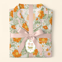 A folded, floral Bouquet Beauty Sage Slumber Party Pajama Shorts Set by The Darling Effect—crafted from ultra-soft fabric in green, orange, and white—is tied with a pale pink ribbon and labeled for a gift-ready surprise.