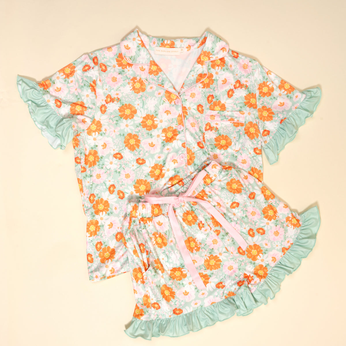 The Darling Effect’s Bouquet Beauty Sage Slumber Party Pajama Shorts Set features ultra-soft fabric, a button-up top, floral shorts with sage ruffled edges, and a pink ribbon waist—perfect for lounging or gifting.