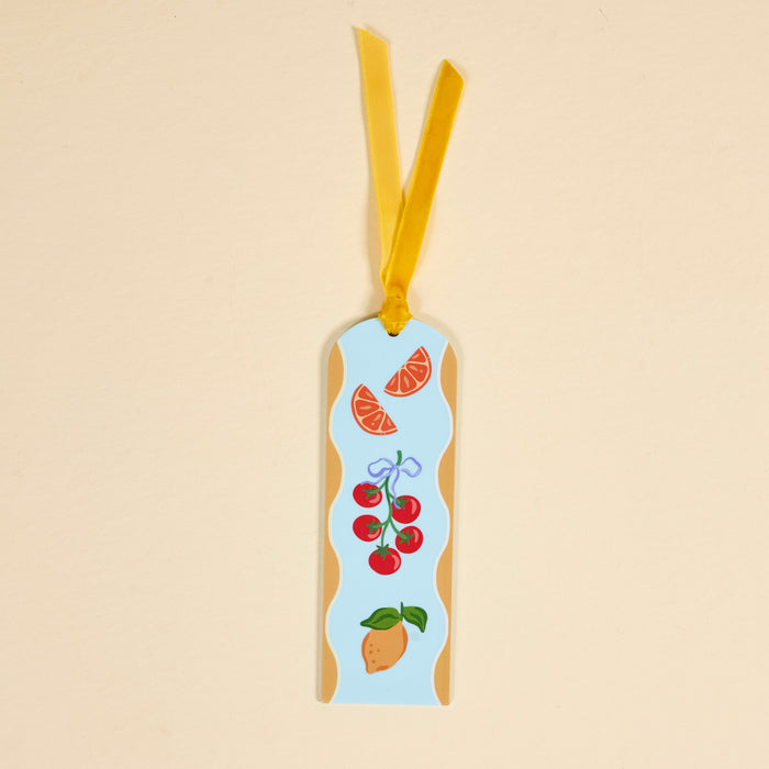 The Fruit Market Acrylic Bookmark features a rectangular shape with a yellow ribbon, showcasing illustrations of orange slices, tomatoes on the vine with a blue bow, and a mango on a light blue background with a wavy beige border—perfect for book lovers.