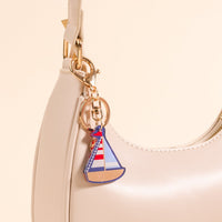 Add a nautical touch to your look with The Darling Effect Sailboat Acrylic Keychain, featuring a red, white, and blue sailboat charm on beige—perfect for accessorizing your cream leather handbag.